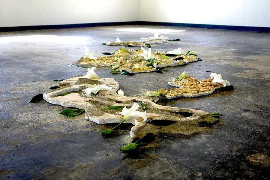 Low sculpture on a concrete floor with white lilies on parts of it