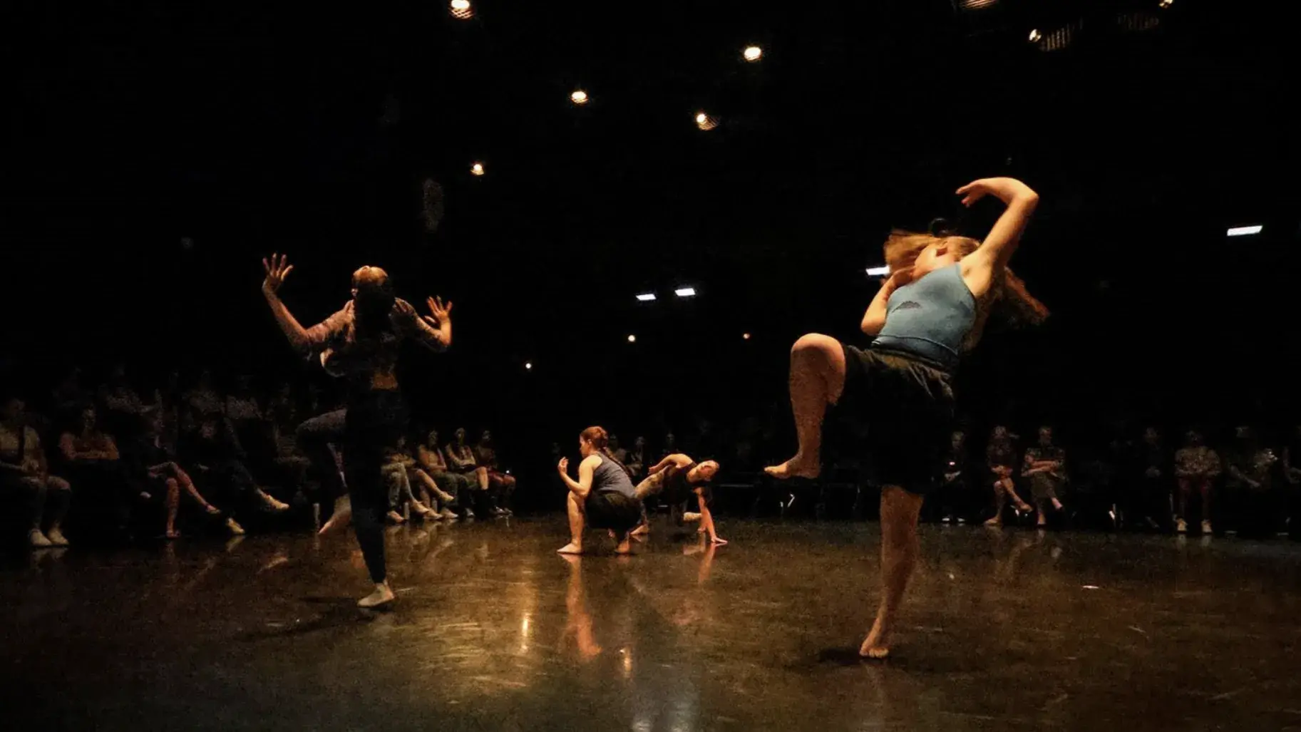 Three ladies acting out a dance on black floor.