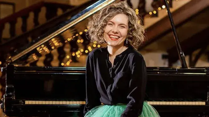 Alexa Stier sitting in front of the piano smiling.