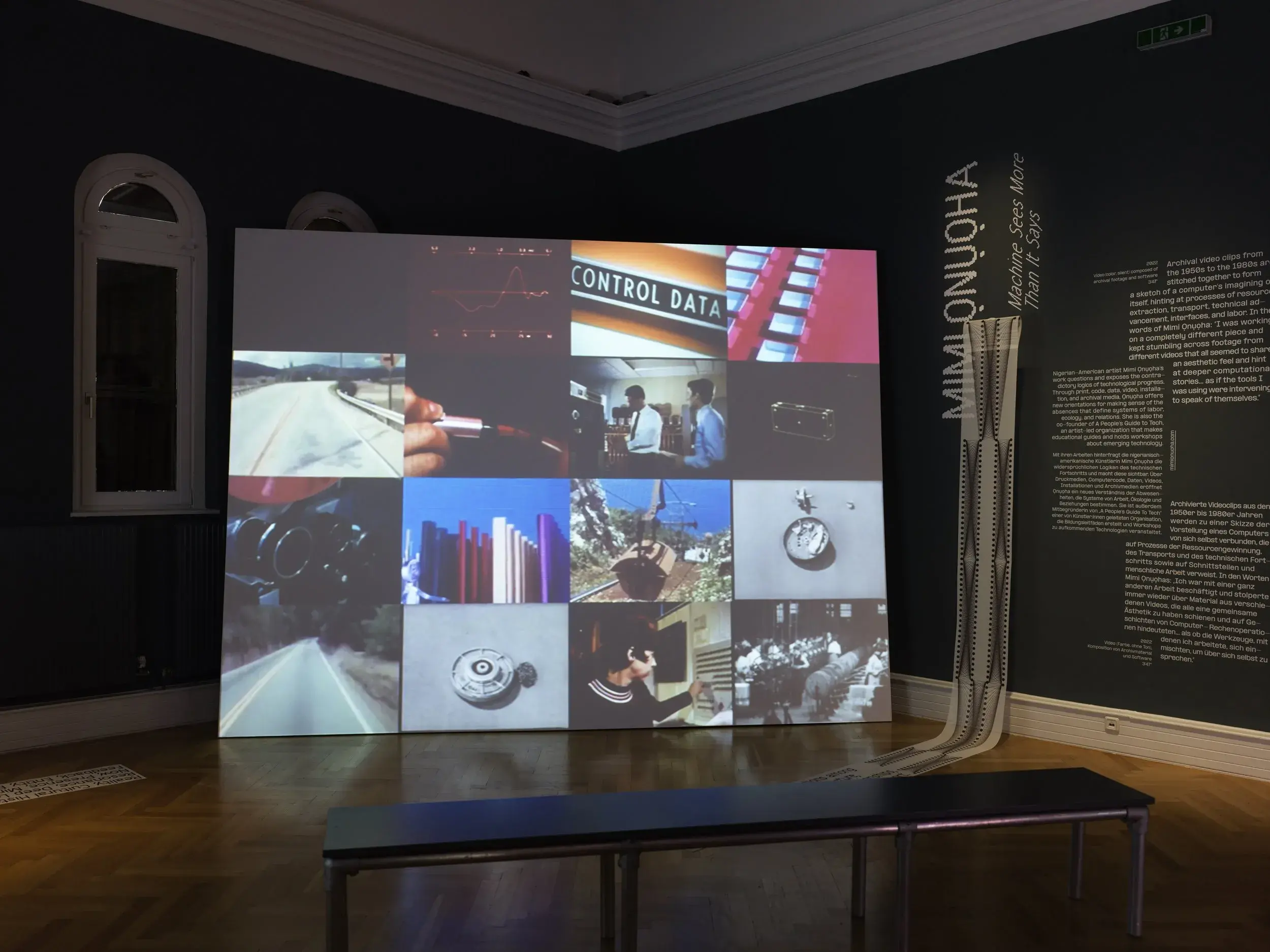 Exhibition installation in a dark room with a screen with a grid of images on it
