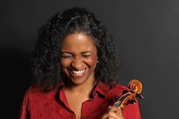 Juliet White-Smith is laughing with her eyes closed and holds a stringed instrumenr