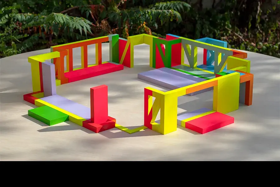 An architectural mock-up. Colorful, geometric design elements are arranged in a square within a courtyard. Trees are in the background.