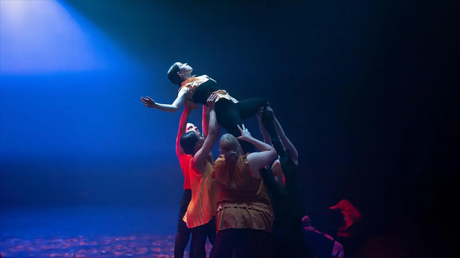 Dancers on stage in a dark space with yellow flower petals on the stage and in the air