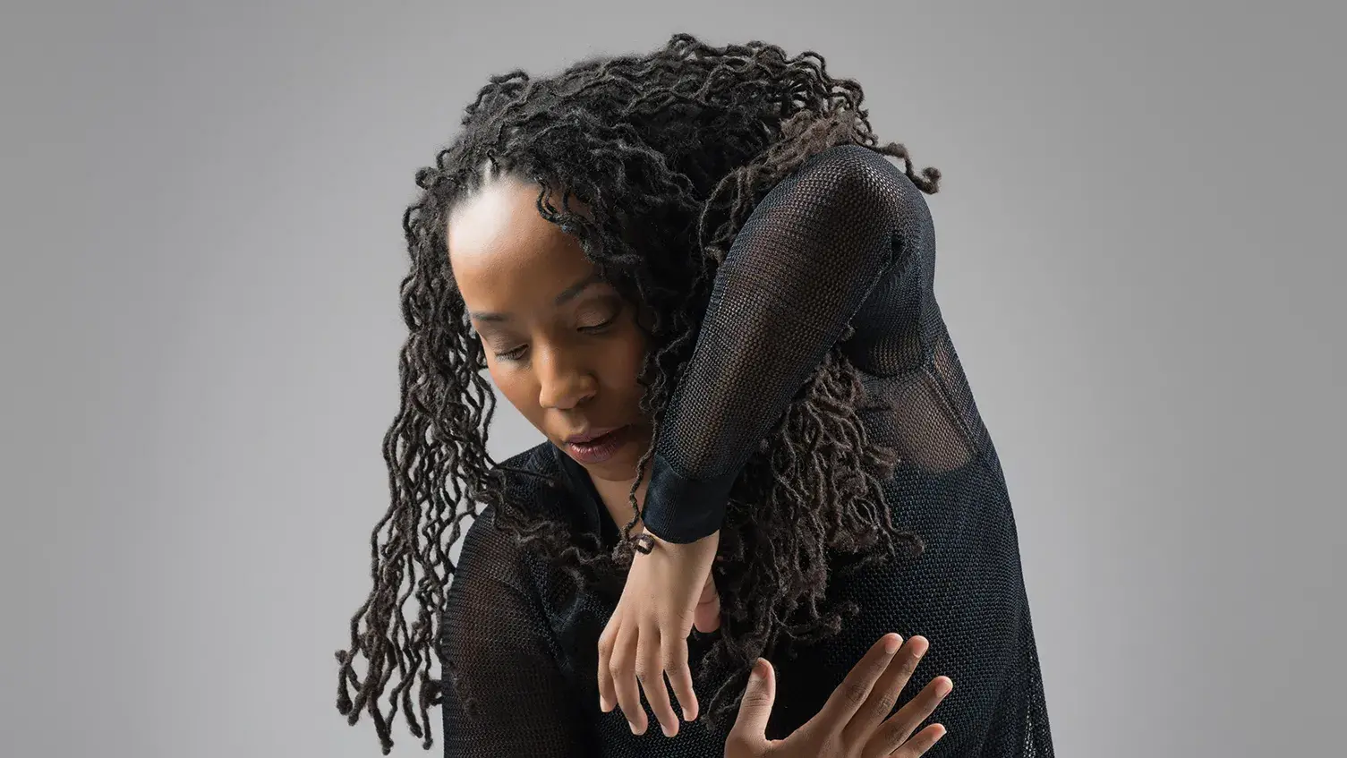 Dancer in all black attire dancing against gray background.