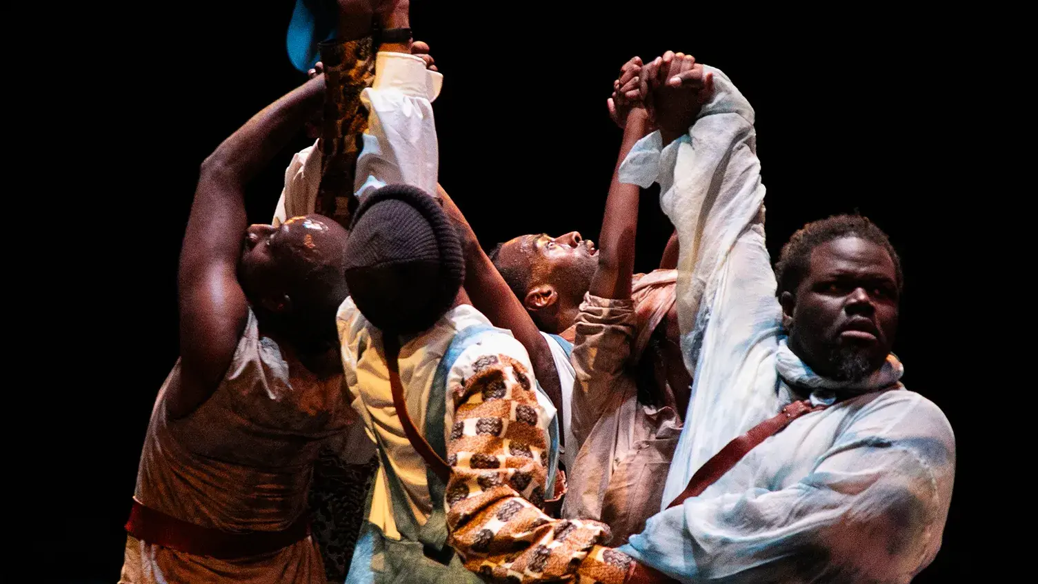 Four dancers with their hands up, looking upward during a performance.
