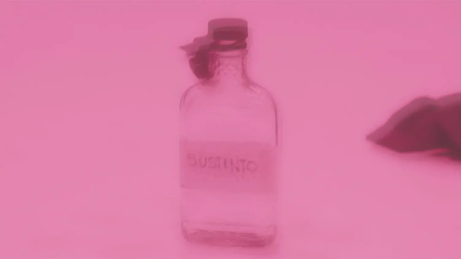 A blurry, pink-tinged image of a clear, lidded sloped shoulder, flattened glass bottle labeled with the word susteno.