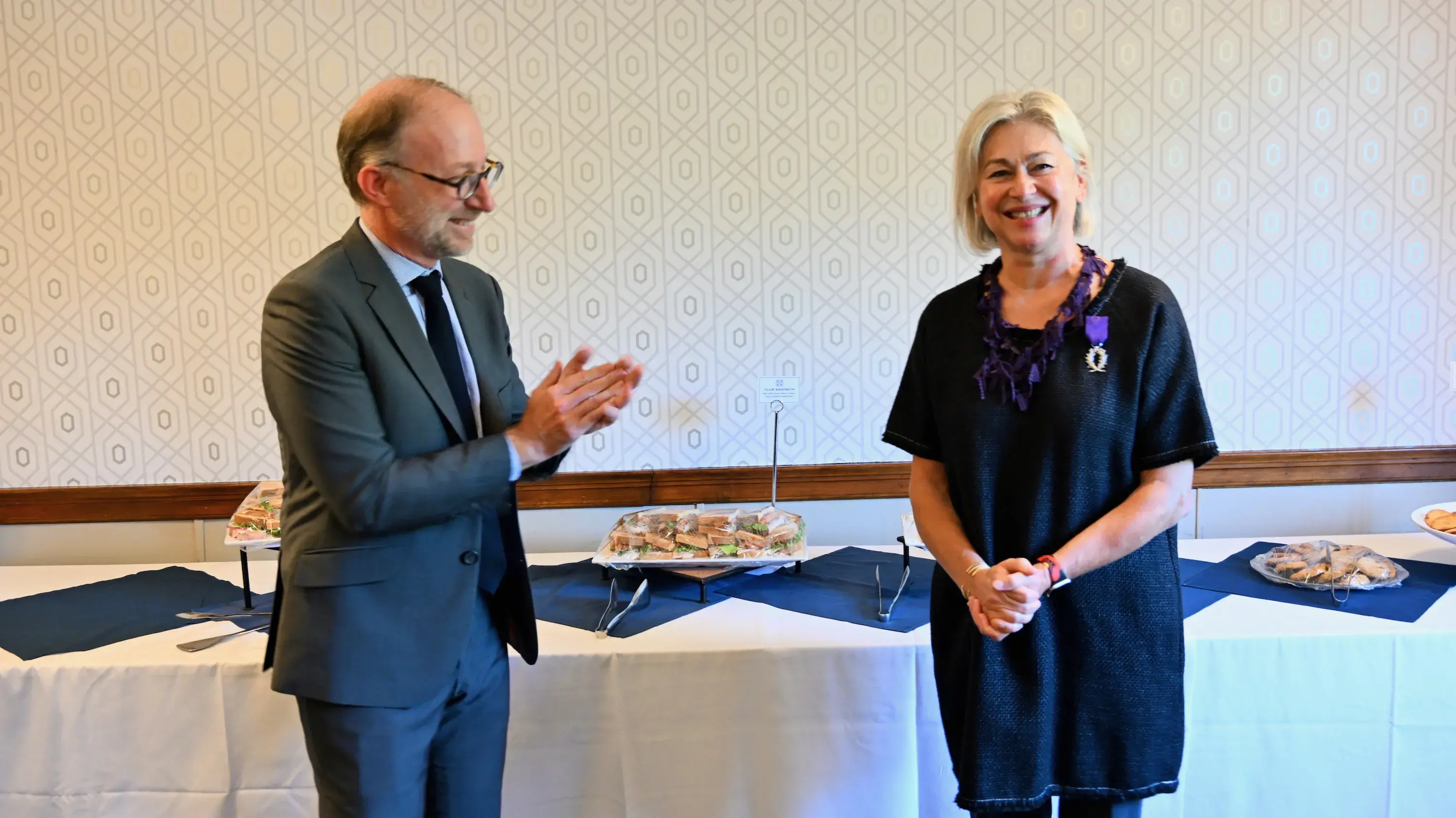 A man in a suit applauds a woman in blue dress