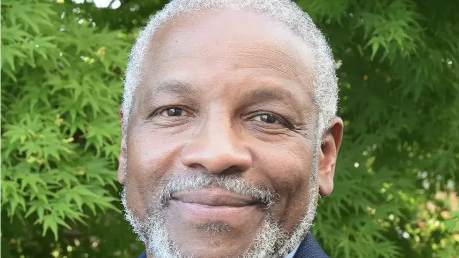 Black man smiling with trees in the background. 
