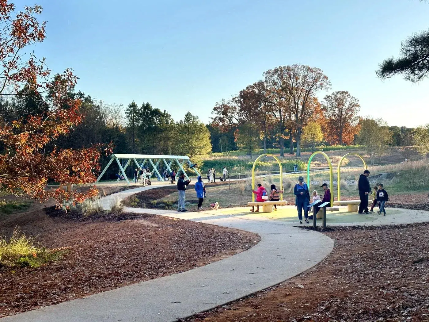 People stand and sit at a colorful playground with benches and swings