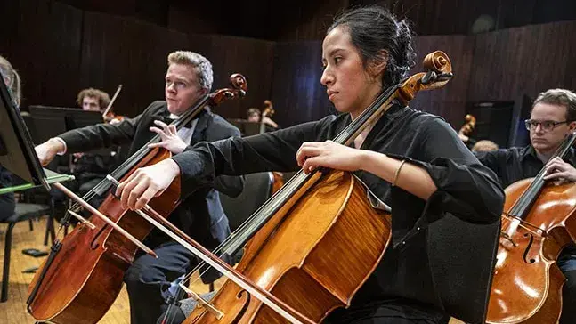 Young people playing cellos while looking at music stands