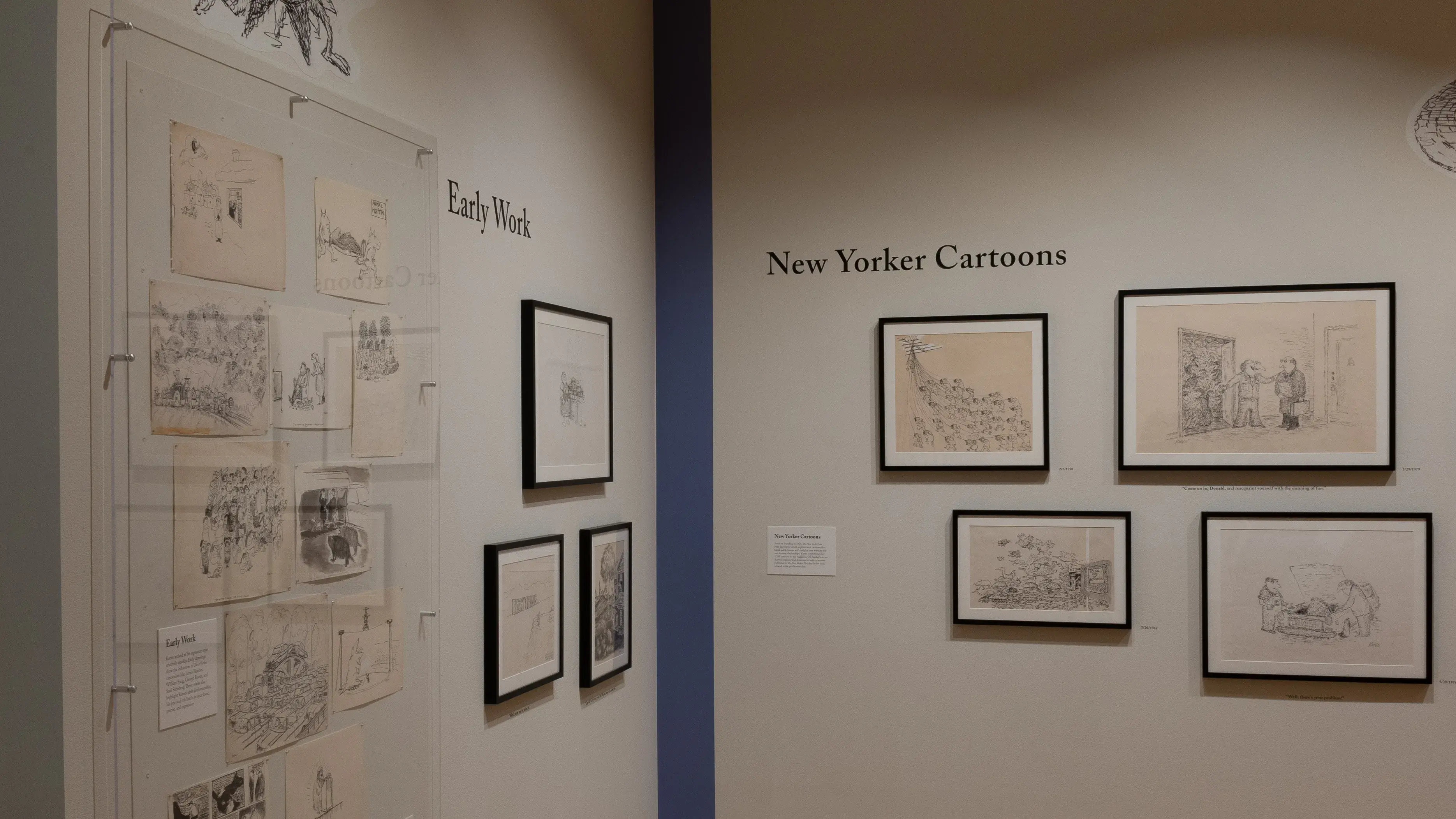 Installation image of a gallery exhibition. There are framed drawings on both walls emerging from a blue corner. Some of the drawings are behind plexiglass.