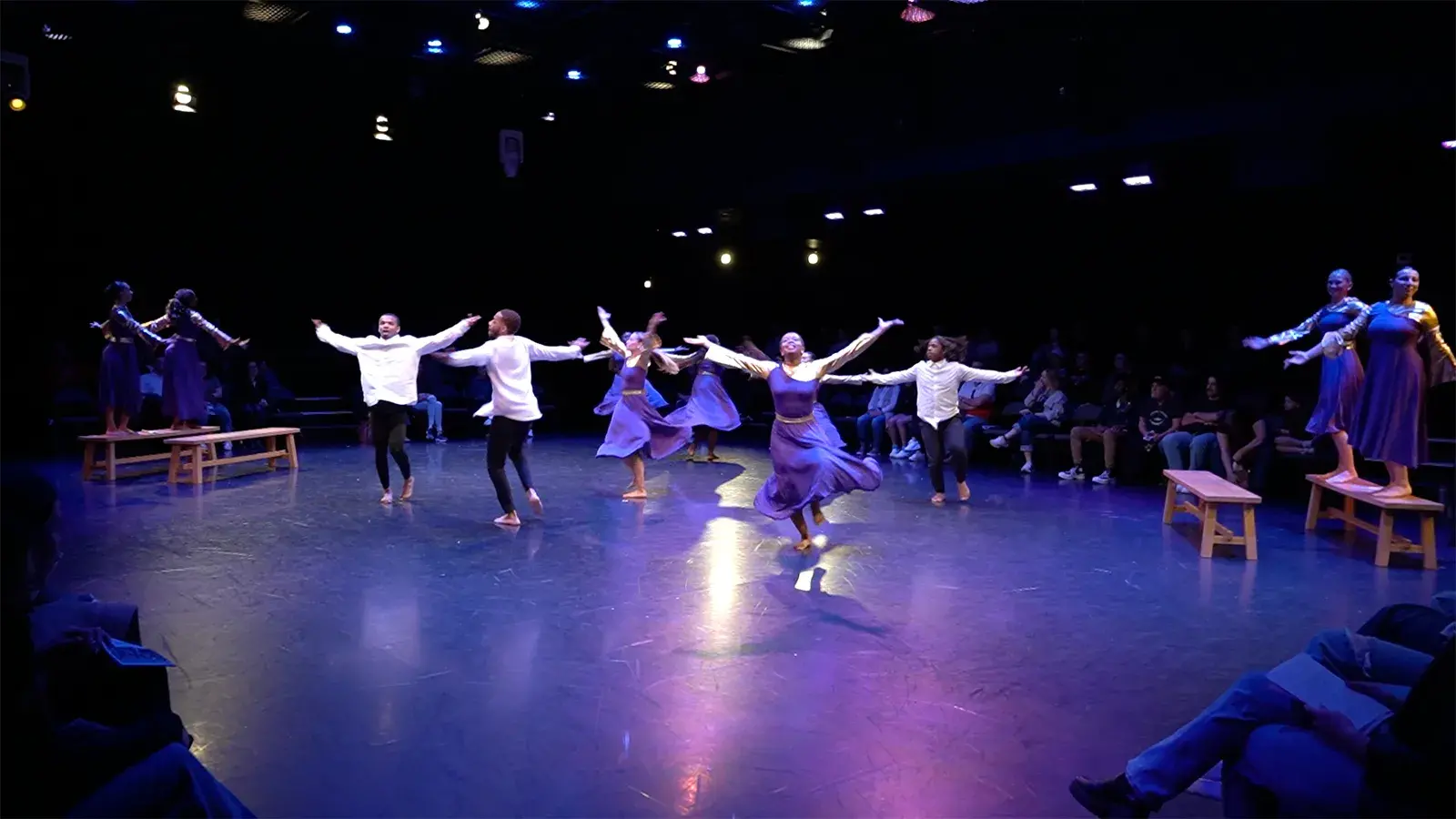 People dancing on a stage wearing purple dress or white shirts and black pants