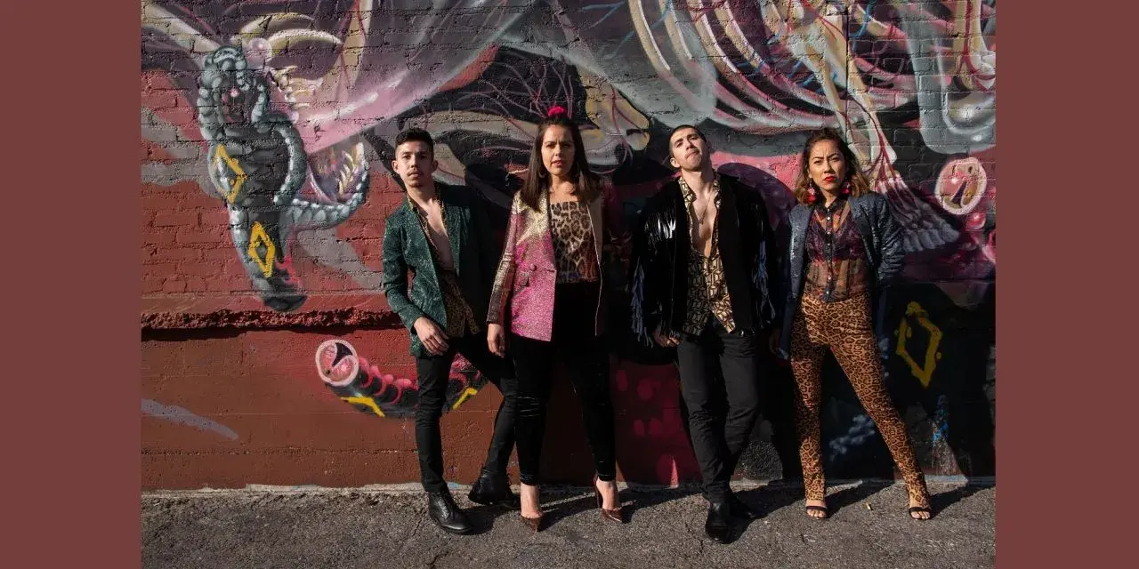 Four people stand in front of a mural on an exterior wall