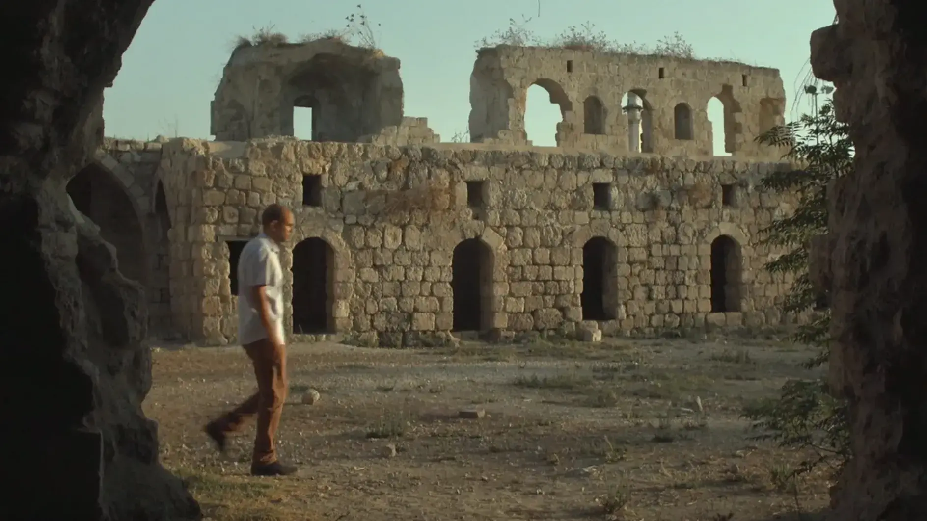 A man walks in front of a stone ruin full of archways.    