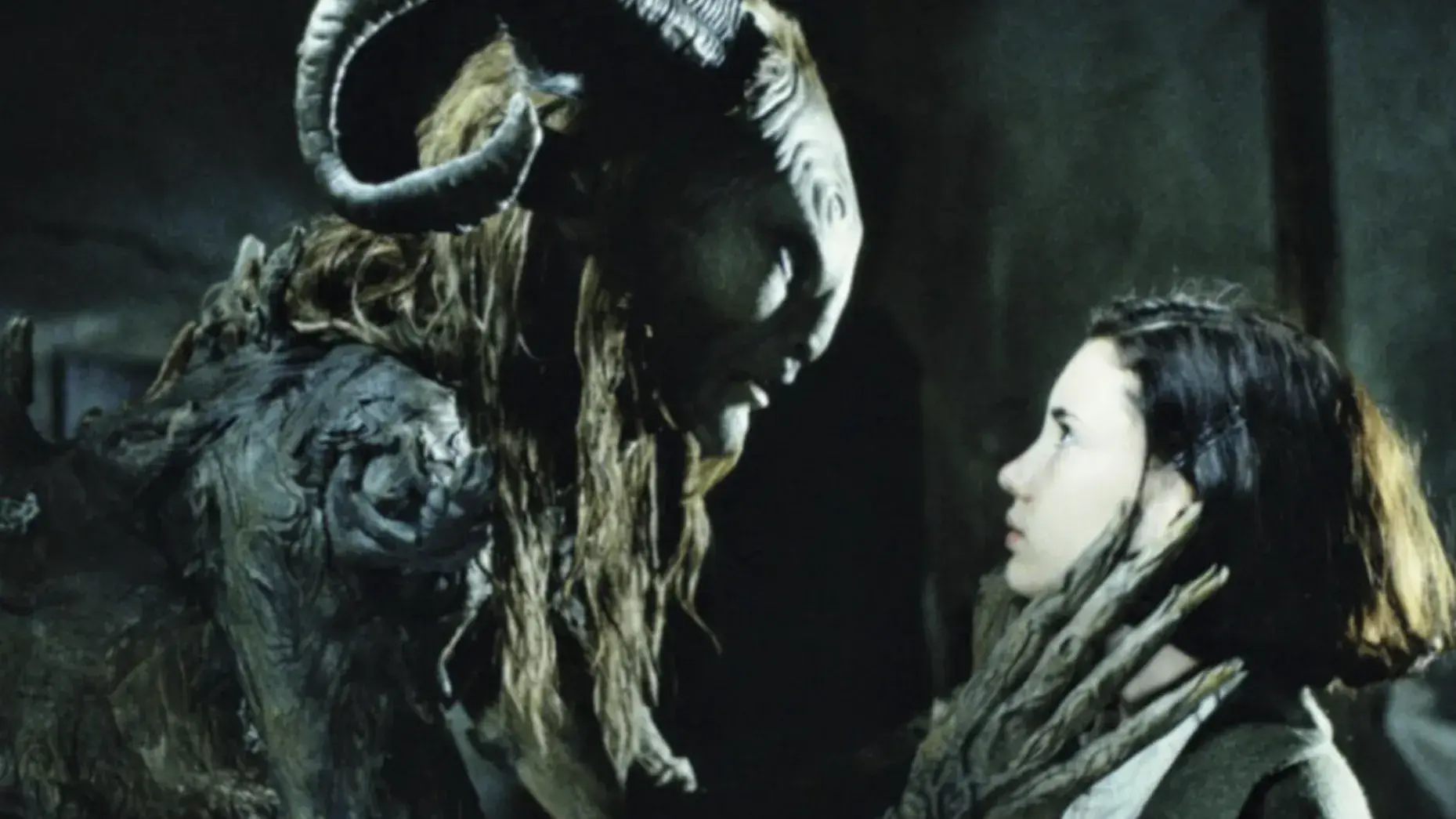 A monster with ram horns and long hair holds a hand with long fingers up to a young girl with brown hair.