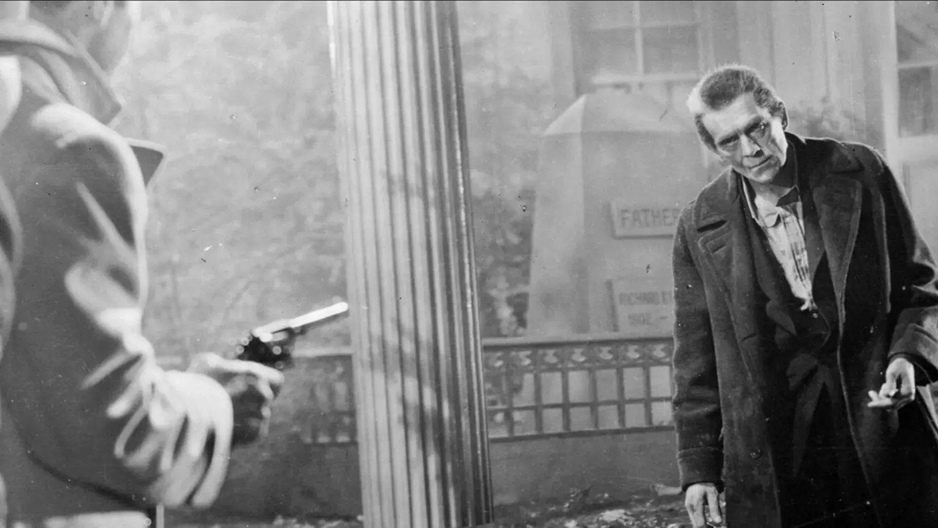 Two men stand in a cemetery pointing a gun at an approaching man. 