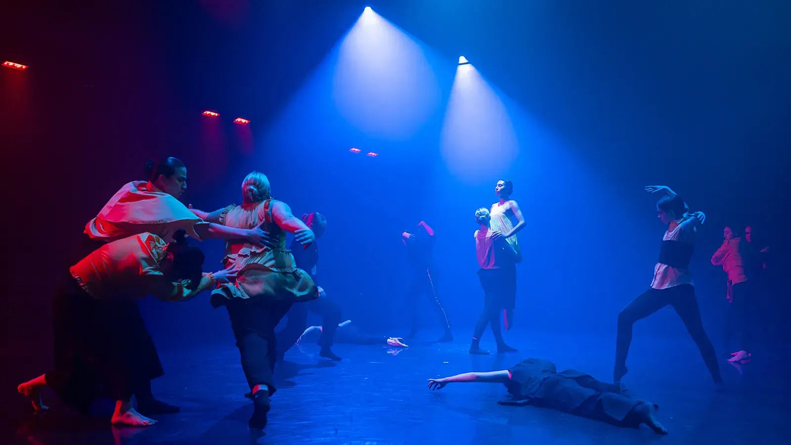 People dance on a stage under deep blue light