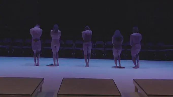 Five dancers standing with their faces in front of an empty audience. 