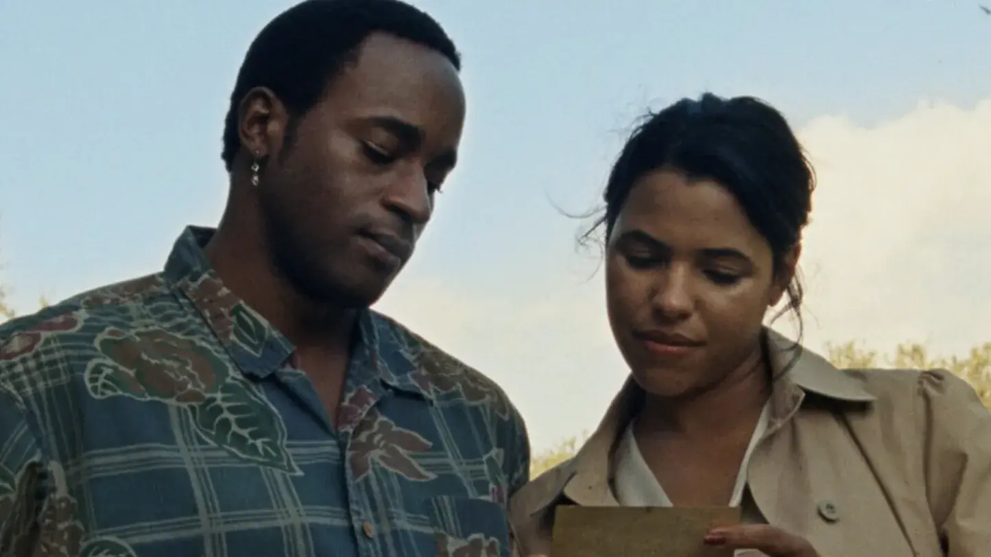 A couple stands outside looking at a photo together. 