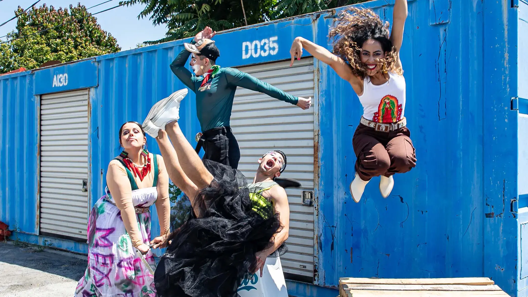 Four people move or jump in front of a blue wall with rollup doors in it