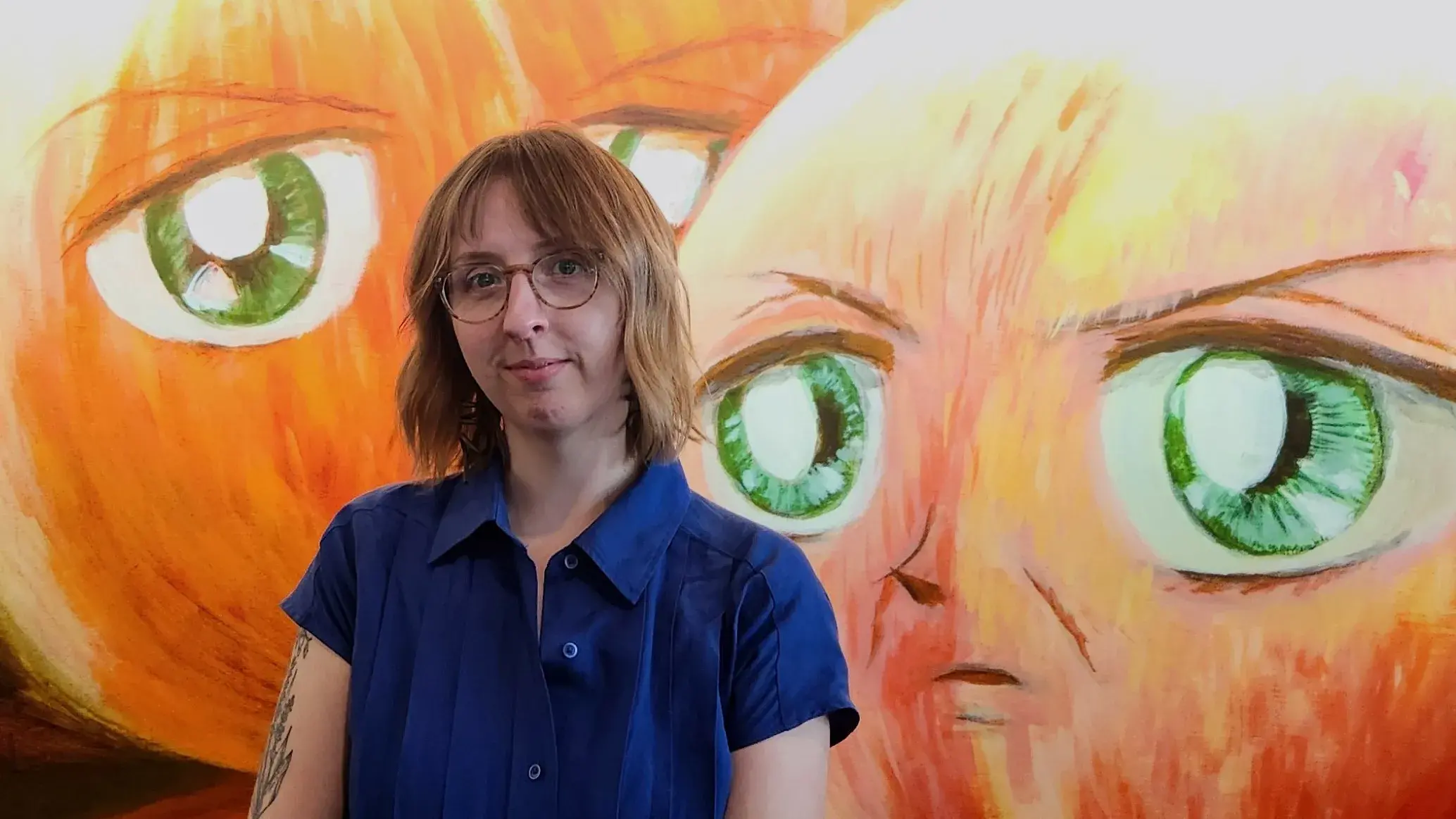 Allie Mickle, a woman with shoulder length hair and glasses, stands in front of a mural.