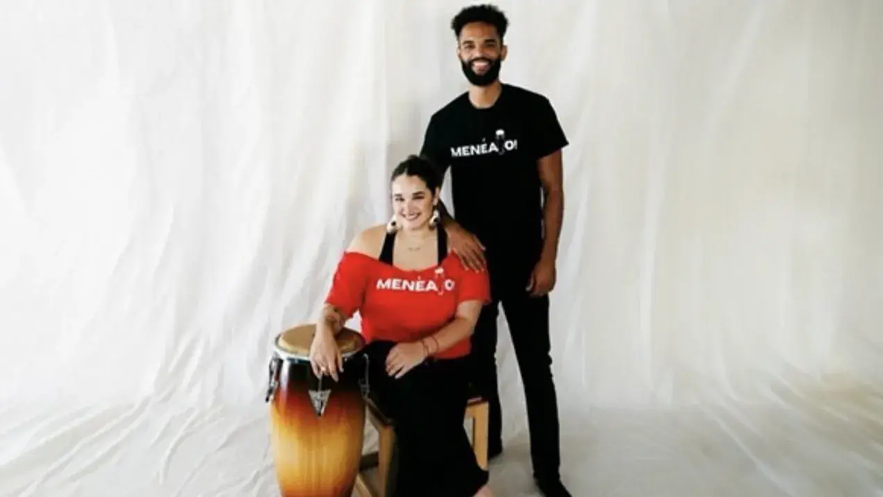 Woman on the left sitting down with arm rested on the conga and man on the right having her arm on woman. 
