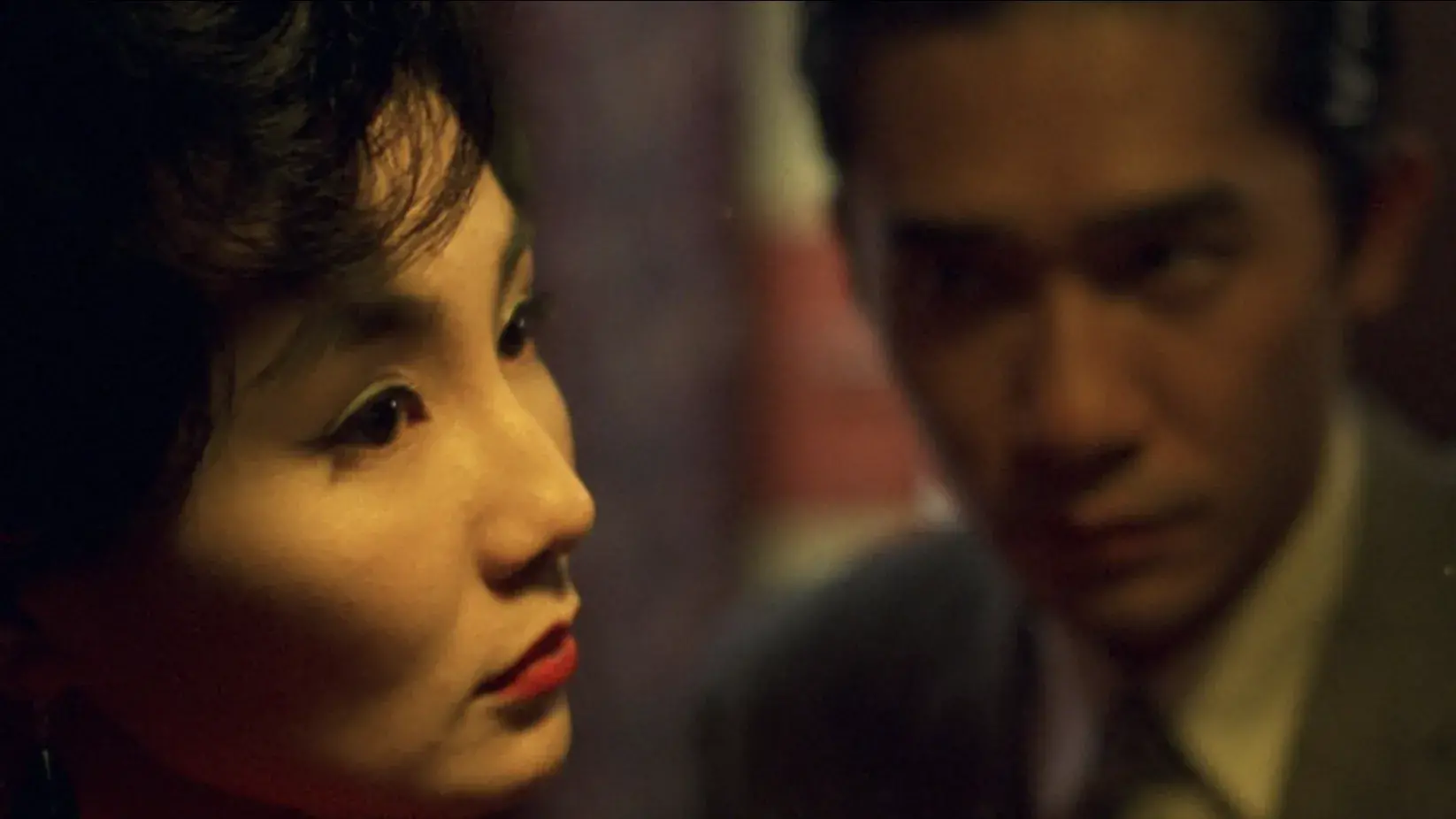 A close up of a woman with a man wearing a suit standing in the background. 