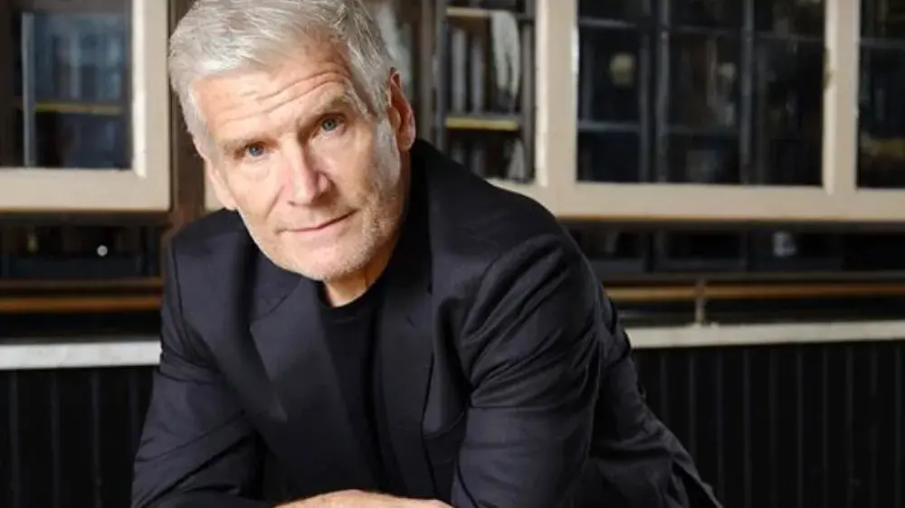 Michael Burritt, a white man with gray hair, wears a black jacket and leans towards the camera