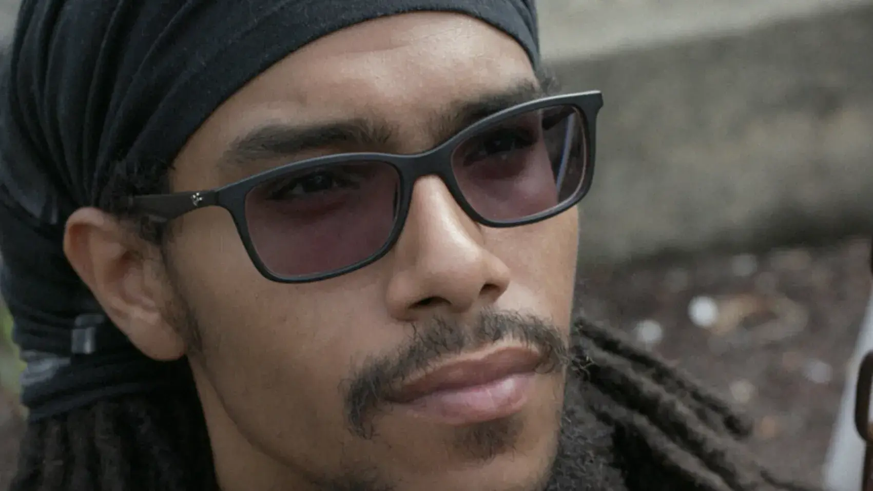 Man with sunglasses and a head wrap sits by a swing chain, looking upwards. 