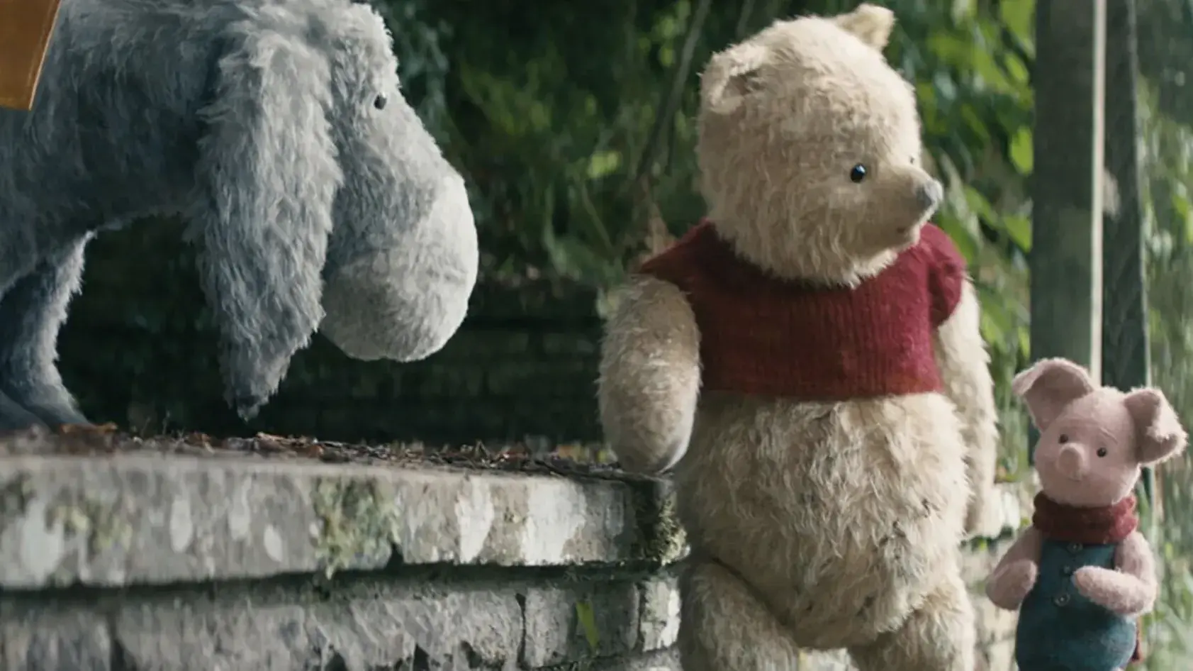 A stuffed toy donkey, a stuffed toy bear, and a stuffed toy pig are standing on a stone wall talking to each other. 