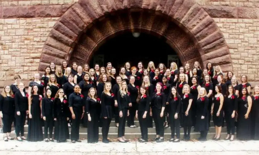 A group of women wearing black stands on steps in front of an arched doorway