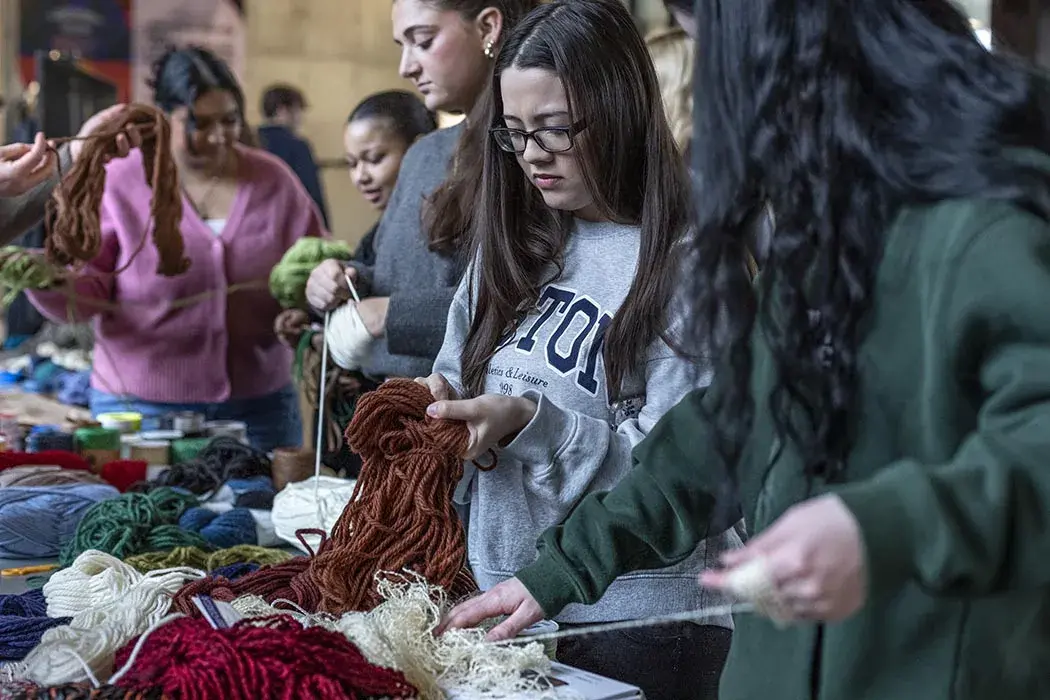 Students stand, touching various colors of thick yarn