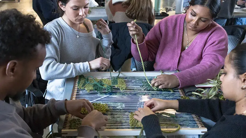 Students weave yarn through a small tabletop loom