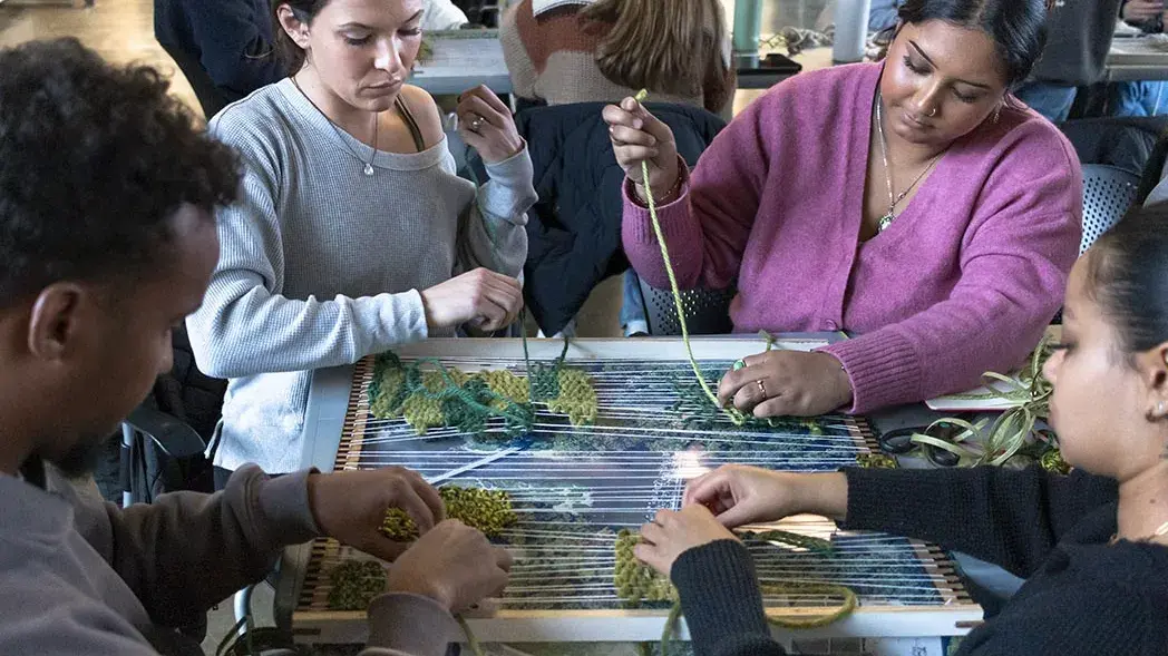 Students weave yarn through a small tabletop loom