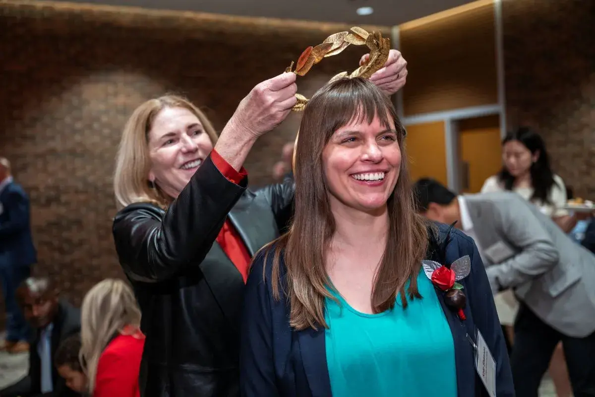 Kate Shannon, a white woman with long straight dark hair, stands while golden laurels are placed on her head