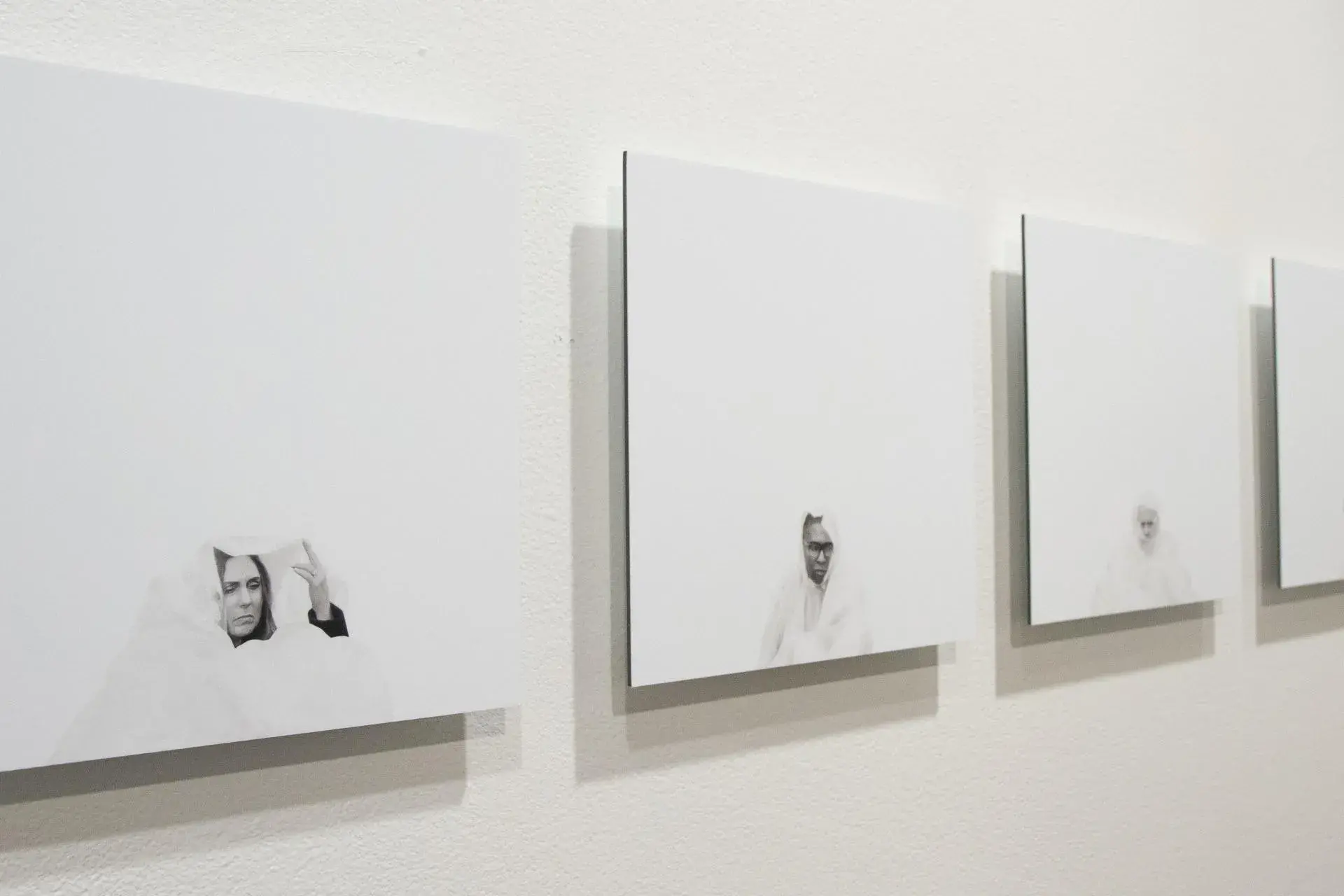 Several photographs on a wall that are mostly white with small faces looking through ripped holes