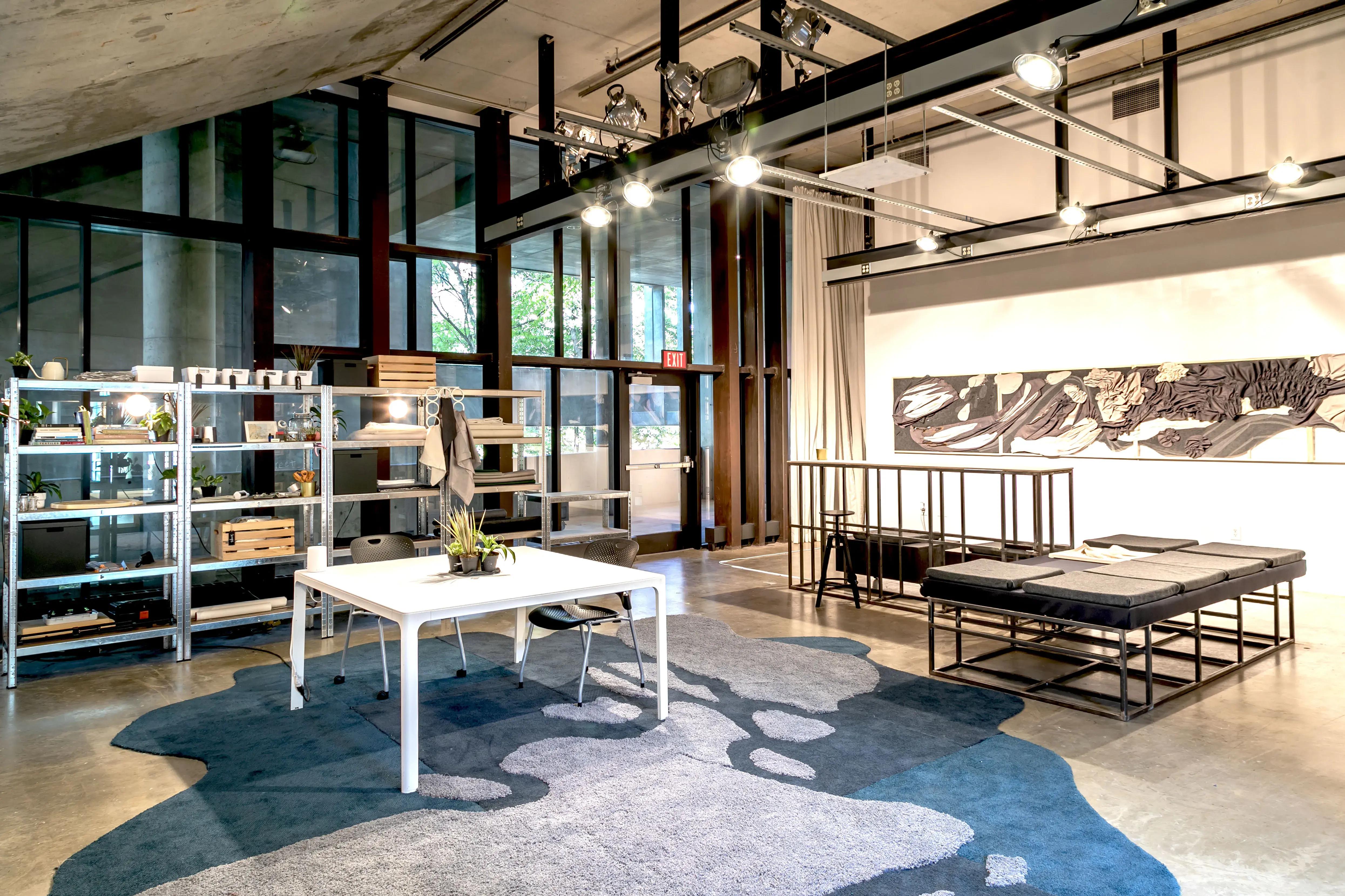 Installation view of an exhibition. There is long grayscale artwork on the wall and tables and shelves with objects on them.