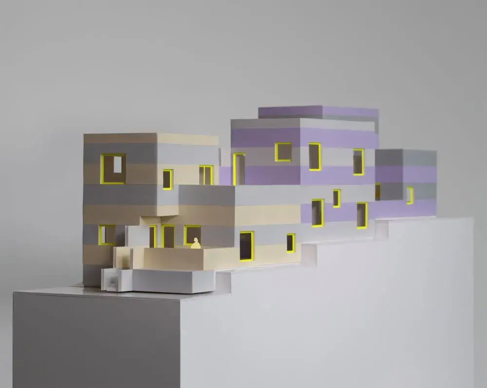 Model of blocky light purple, gray, and light yellow building on a tiered base