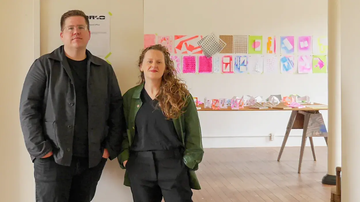 Outpost Office Erik Herrmann and Ashley Bigham stand together in front of a wall with bright colored pages on it