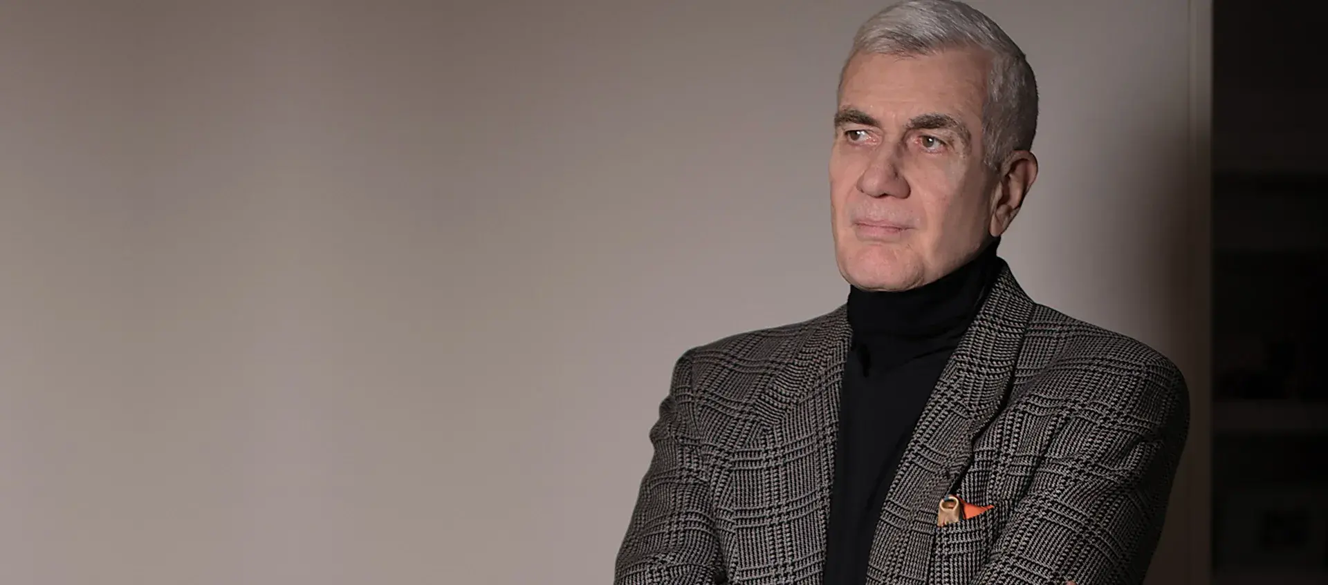 John Canemaker looks away from the camera. He has gray hair and wears a black turtleneck and a gray blazer