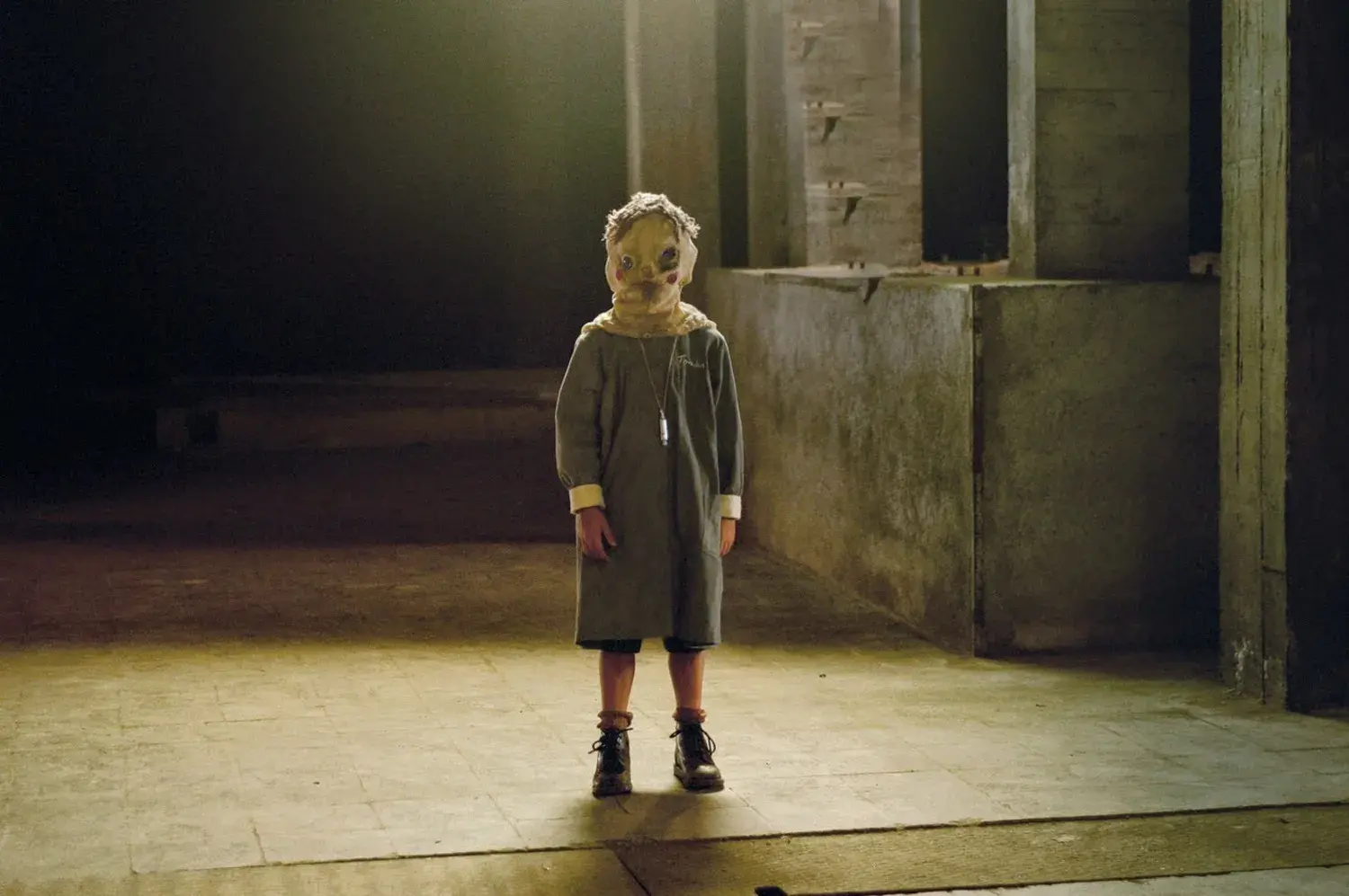A child is standing in a dark room with a spooking mask over its head.