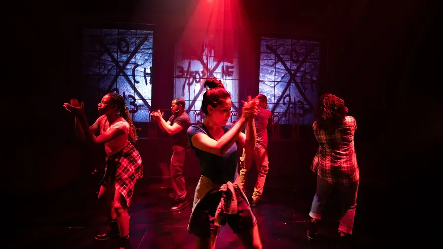 People dancing on a darkened stage with red lights