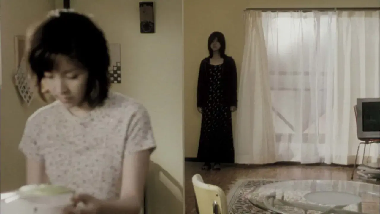 A woman is standing in the foreground in a light-colored room with a woman in a black dress staring at her in the background.