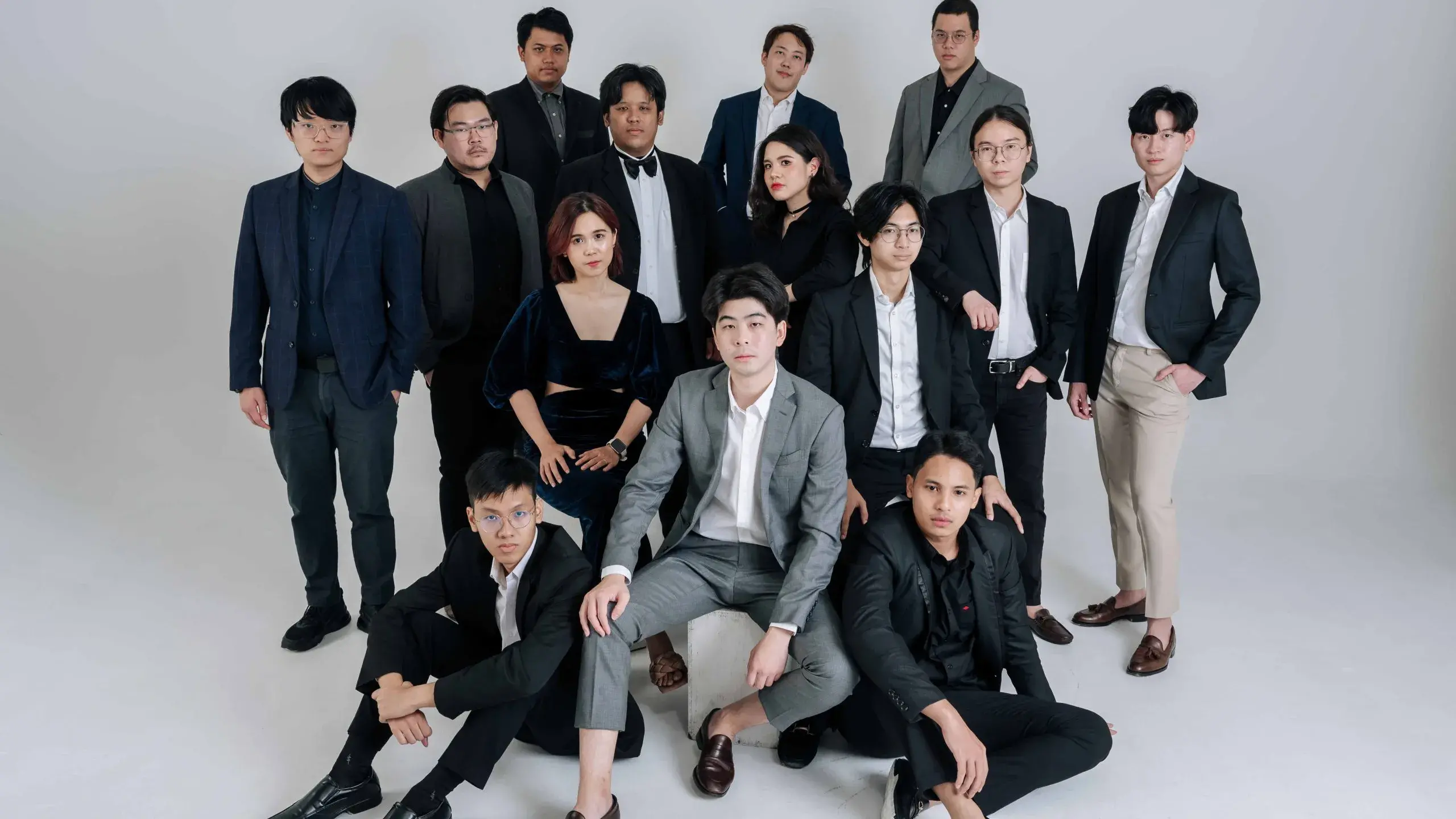 A group of young Asian people stand and sit together against a light backgound