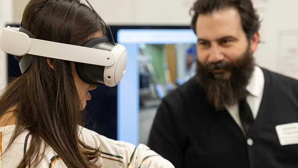 A young person with a Virtual Reality headset on stands in front a man