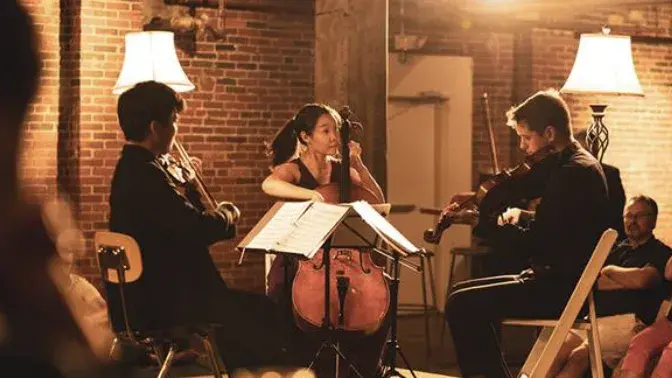 Two men and a woman performing a orchestral piece in front of a audience. 