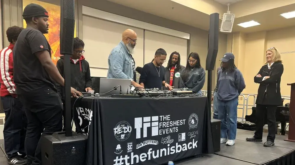 Several people stand and next to a DJ table