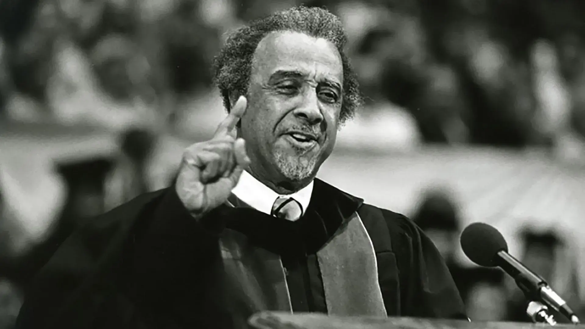A Black man stands at a podium and gestures while making a speech