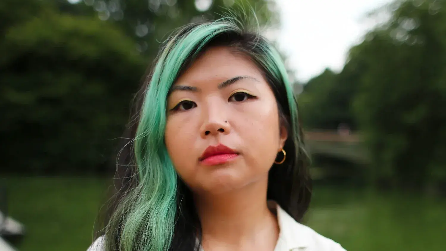 Headshot of Gina Chung who is standing outside and has a stripe of green hair near her face