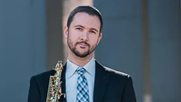 Michael Rene Torres holds a saxophone and smiles at the camera